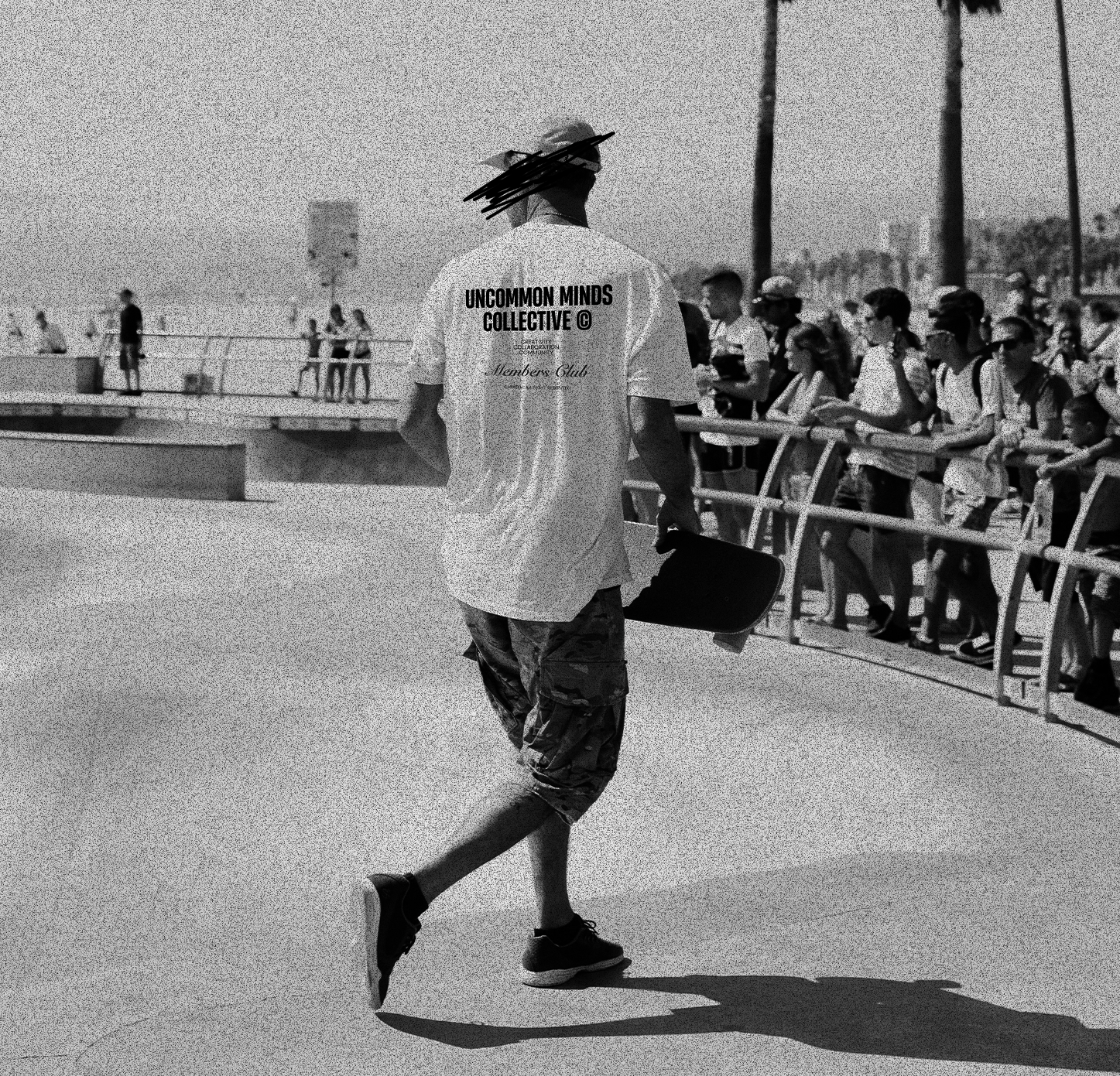 Man with skateboard photographed from the back, wearing a white t-shirt by Uncommon Minds Collective (UMC). Urban streetwear style for skaters, featuring minimalist design and casual fit. Shop UMC for skater-friendly fashion.