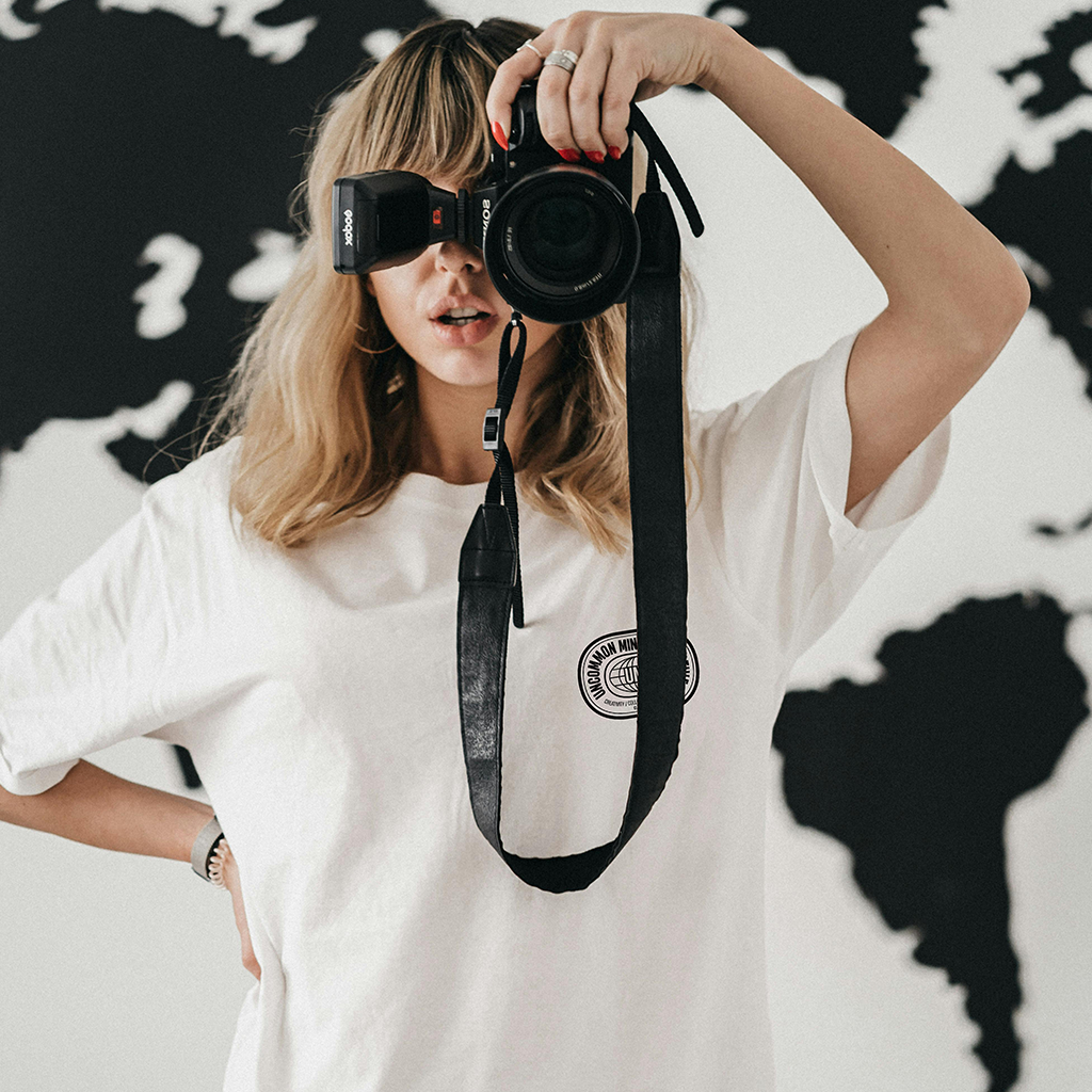 Woman holding a camera, wearing a white t-shirt by Uncommon Minds Collective (UMC). Stylish and minimalist streetwear for women, perfect for casual photography enthusiasts. Shop UMC for trendy and comfortable fashion.